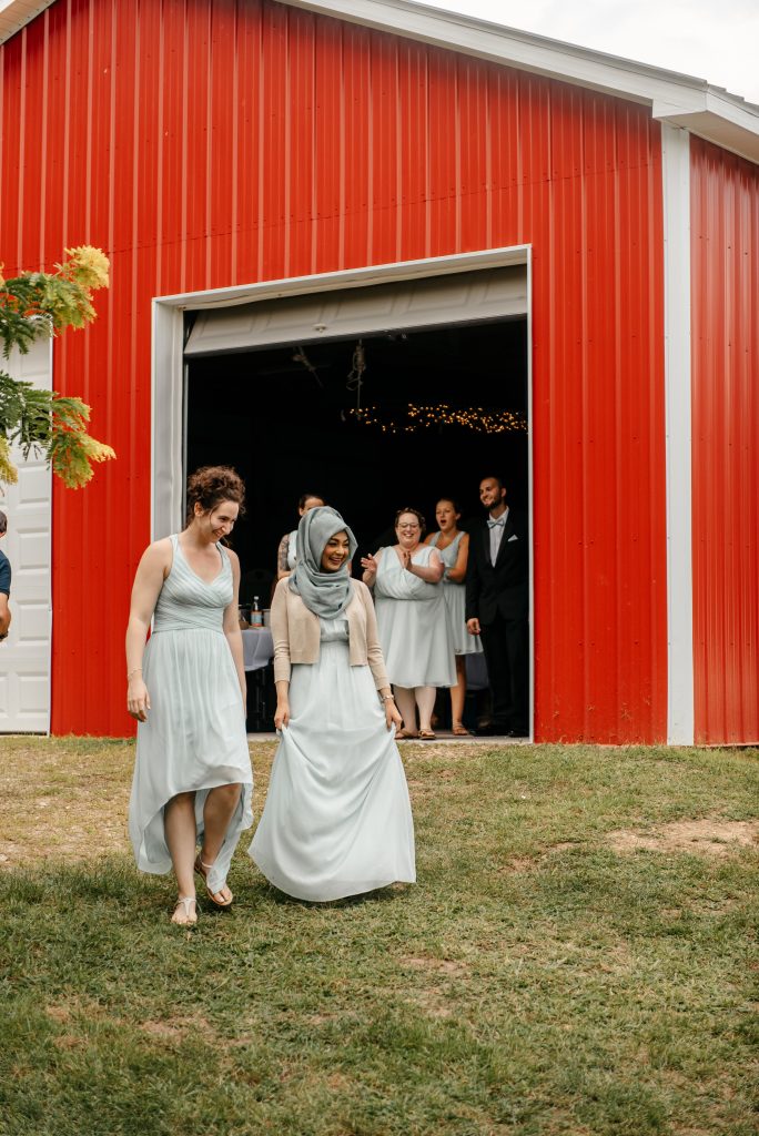 Two bridesmaids walk down a hill from a red barn to a reception area where their friends have learned the getting married in new york requirements