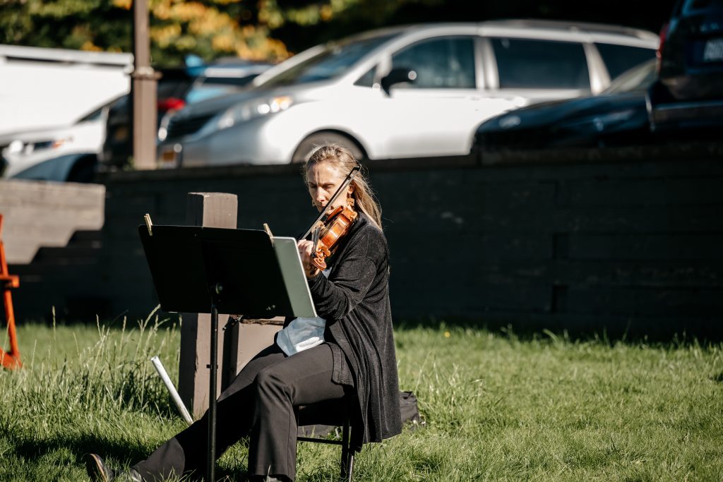 A woman in black plays the violin while reading music at an outdoor venue for a couple who learned the
average wedding cost upstate ny