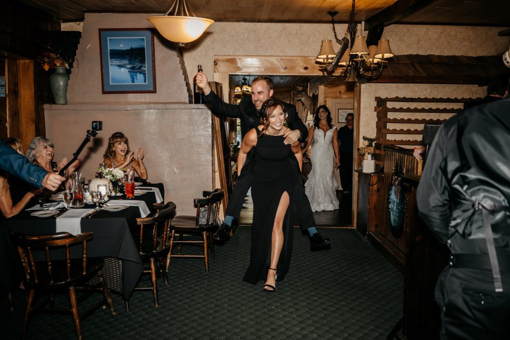 A bridesmaid carries a groomsman into the reception venue because their friends are getting married knowing the average cost of an upstate ny wedding