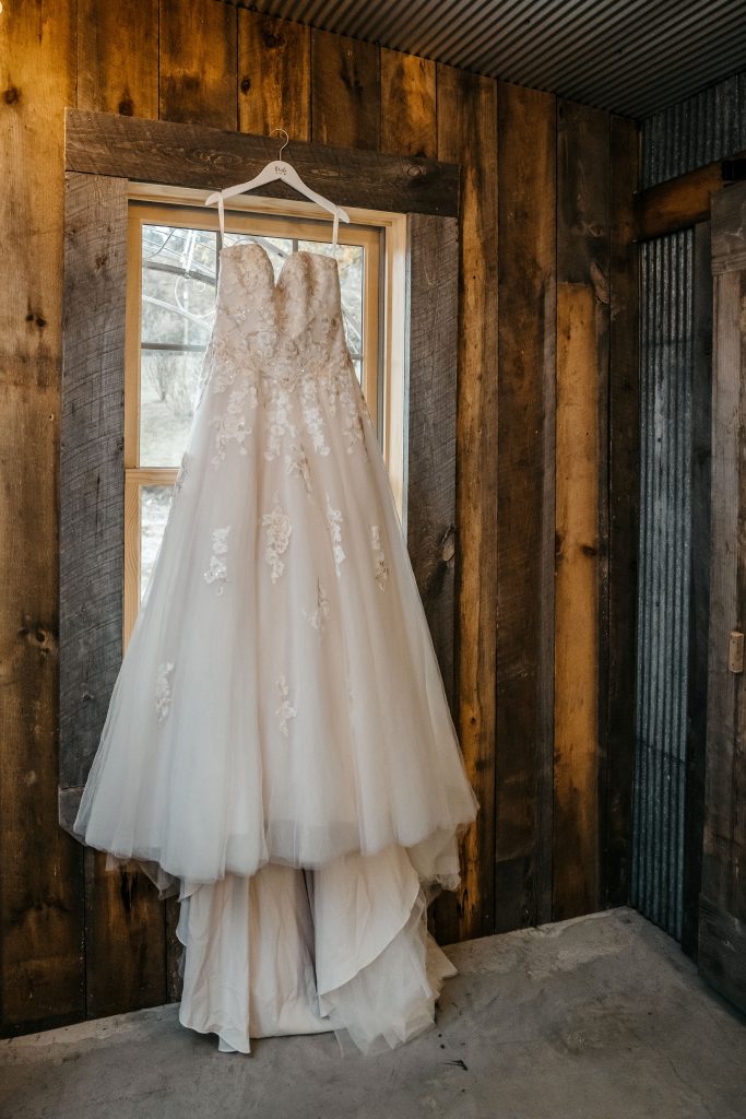 A bride's wedding dress hangs in a rustic window of a washington county wedding venue