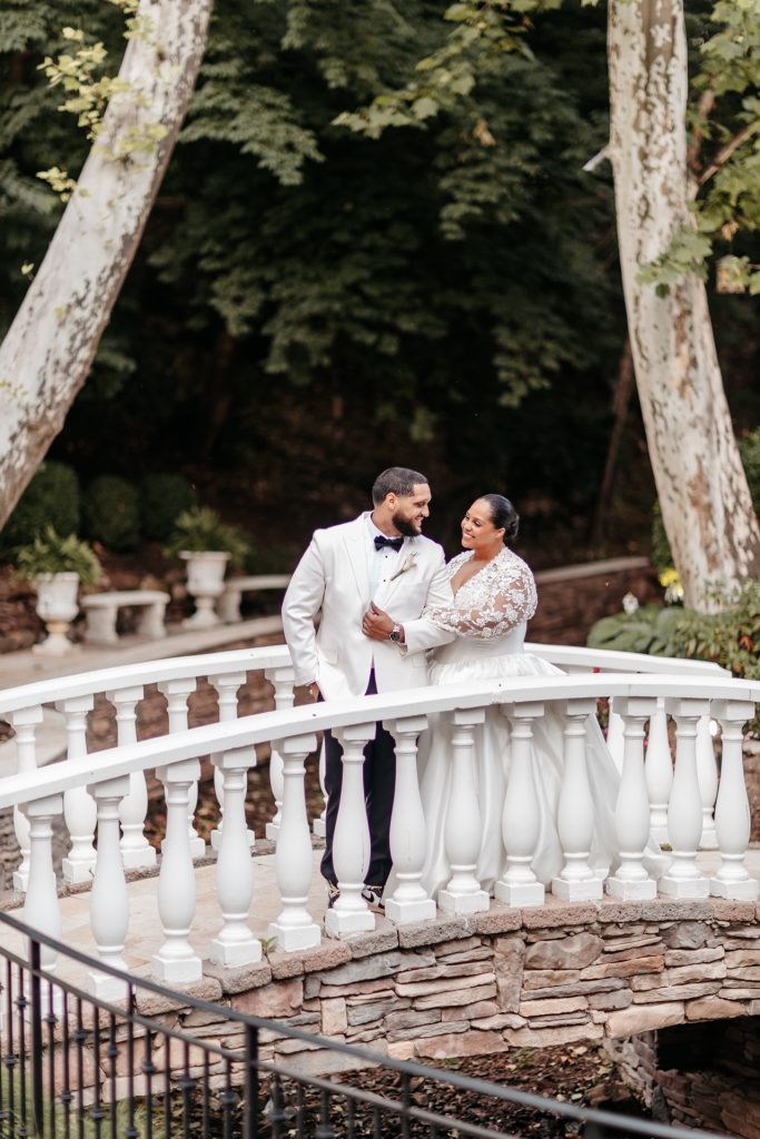 A couple stands on a small white bridge and smile wondering what is the best month to get married in Upstate NY