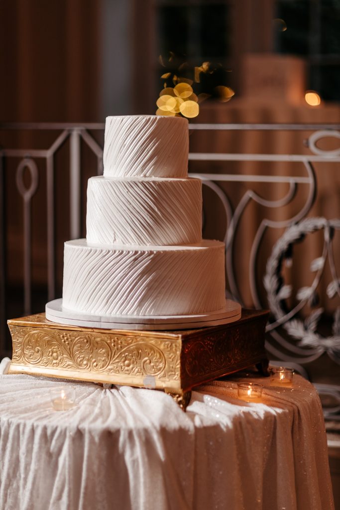 A beautifully decorated three-tiered wedding cake stands on a golden platform for wedding photos in new york
