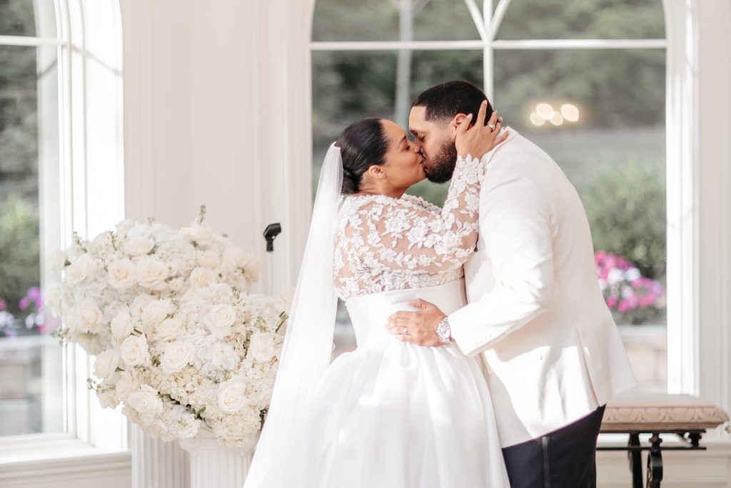 A bride and groom kiss in front of a window and white bouquet for theirwedding photos in new york
