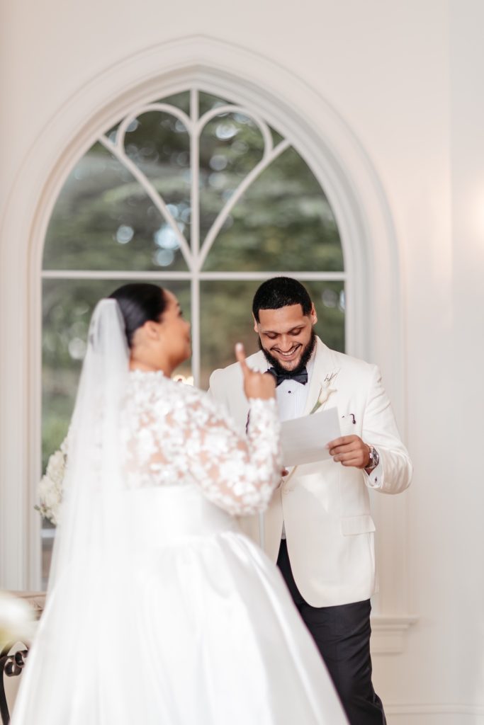A bride points to the sky and smiles as her groom reads his vows in their new york wedding photos